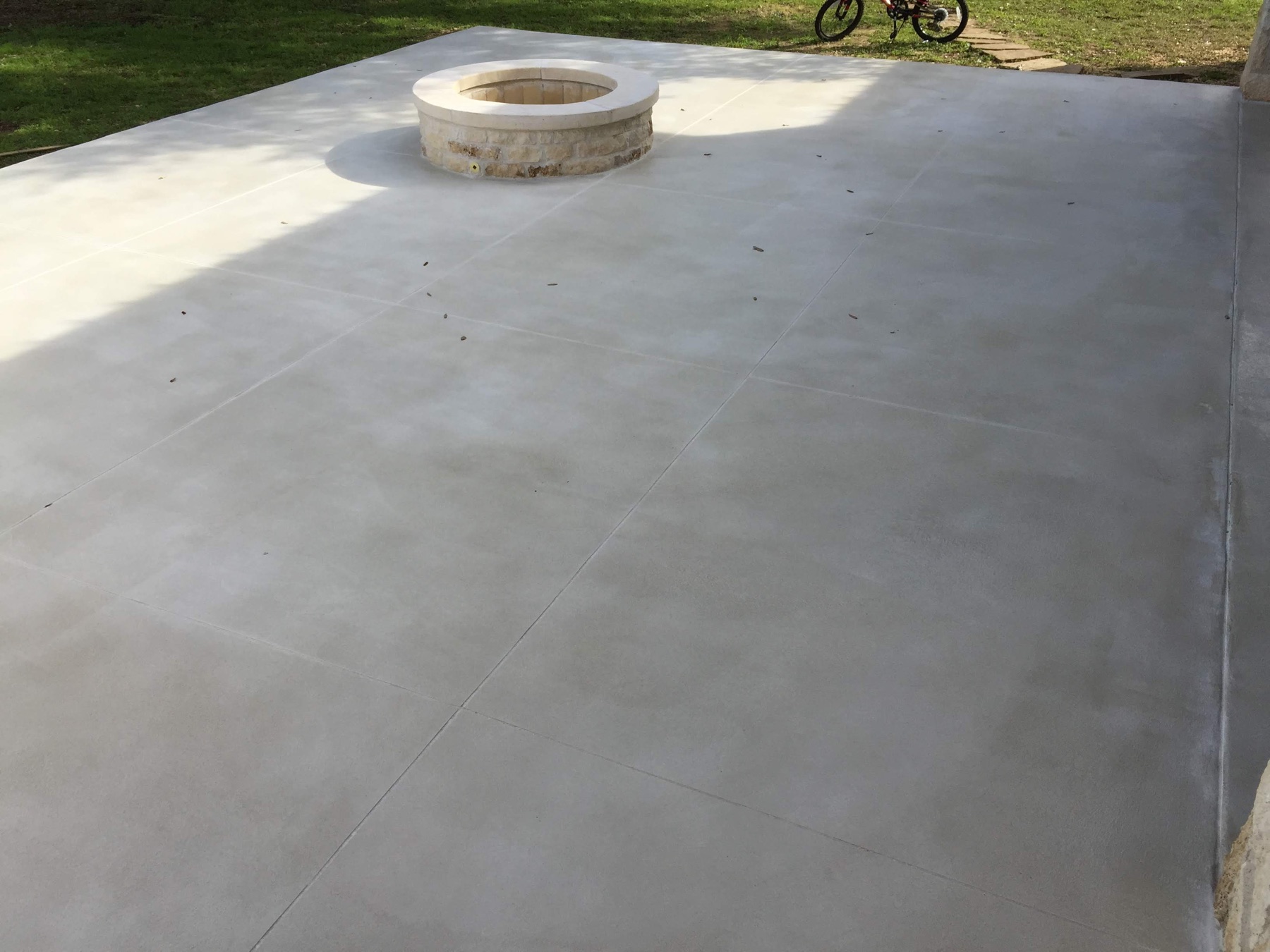 Completed light gray PetraBroom patio with scored joints around a circular stone fire pit